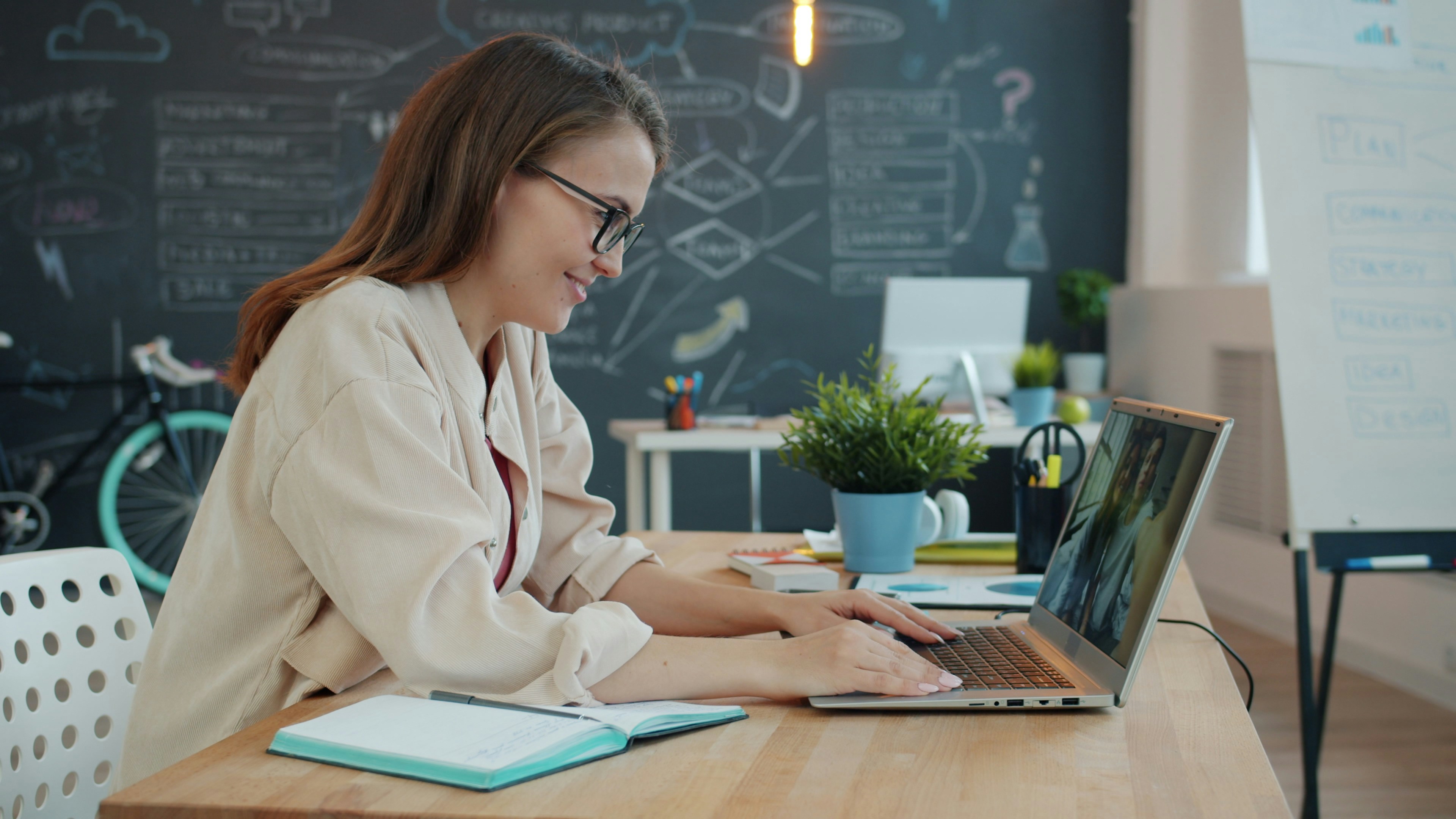 A learner engaging in online learning course on a laptop, with notes open on a desk.