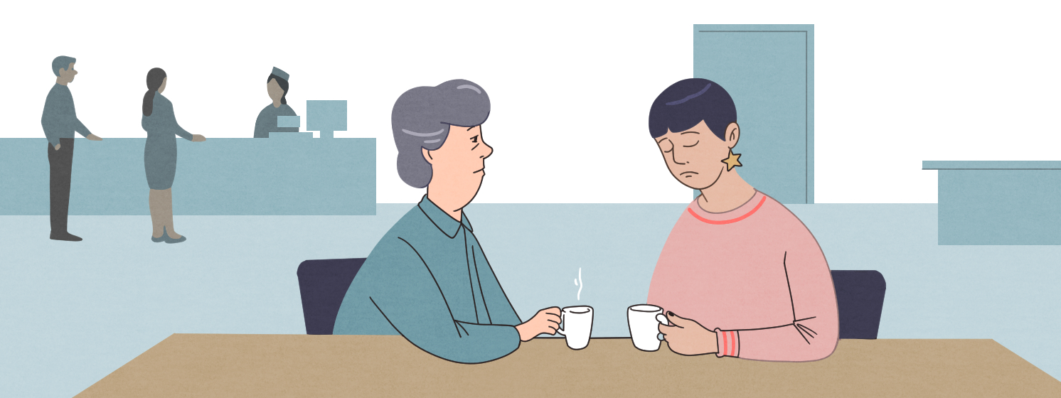 Supportive one-to-one conversation - both seated at a table with hot drinks.